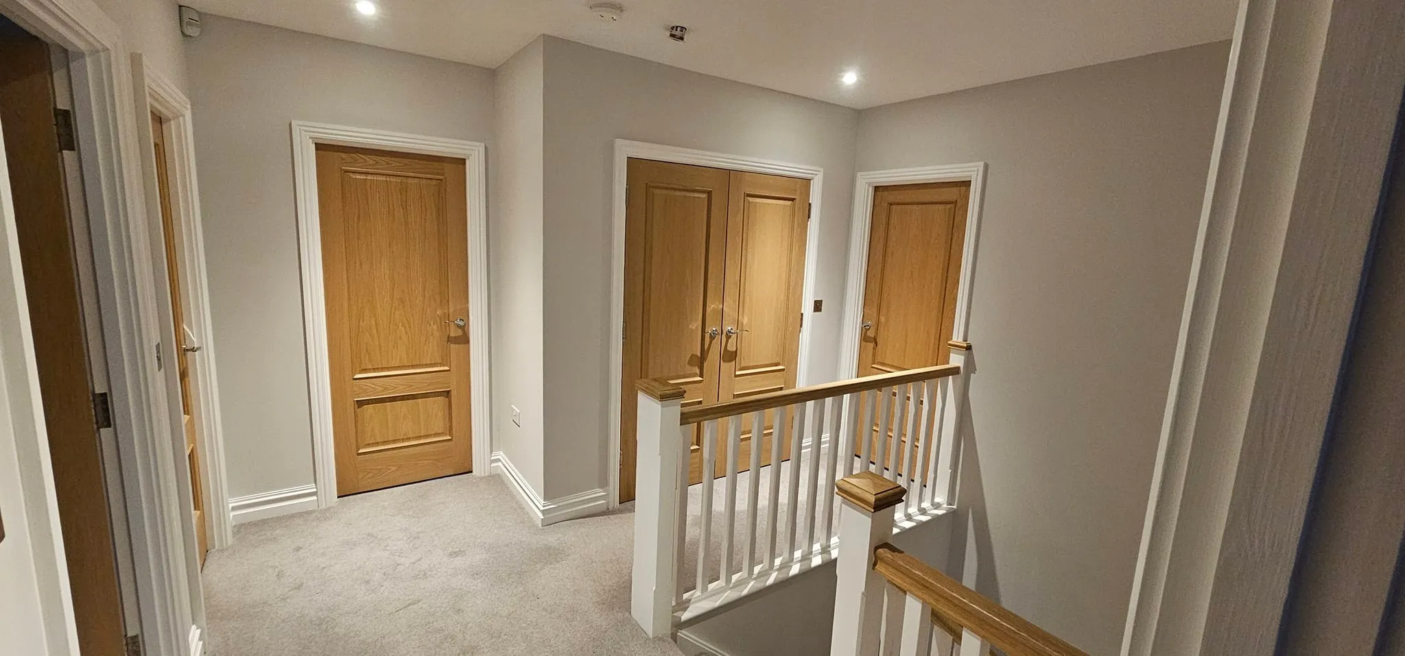 An empty hallway with wooden doors and white railing.