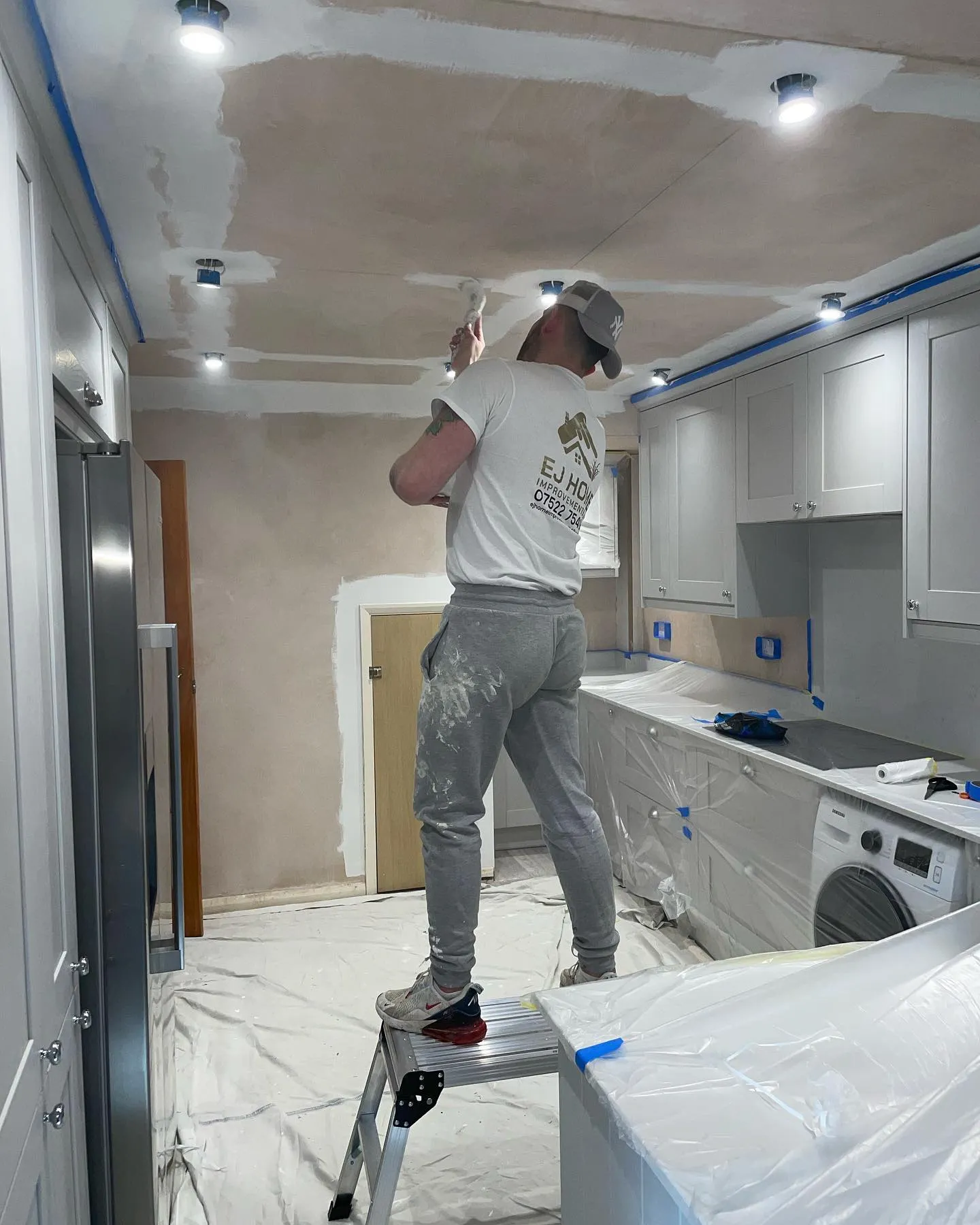 A man standing on a ladder painting a kitchen.